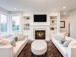 Two white couches facing each other in a living room with a tufted ottoman in the middle of the room