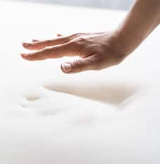 Hand hovering above a white memory foam mattress with a hand indentation